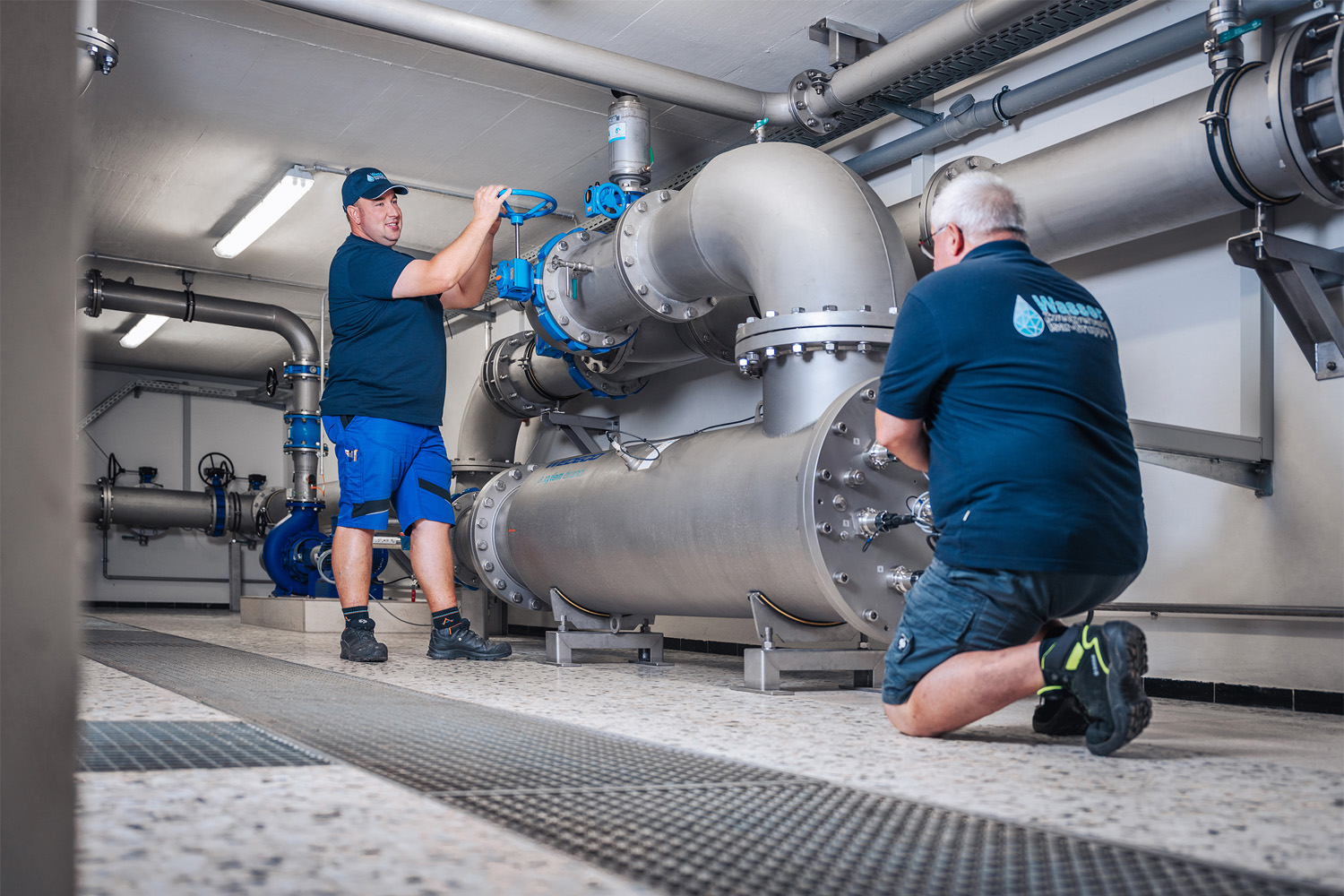 Zwei Mitarbeiter warten die Rohrleitungen und Armaturen im Wasserwerk